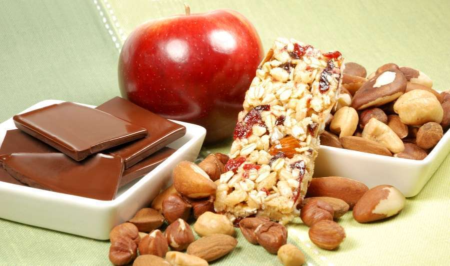 granola bar, nuts, apple and chocolate on a green surface