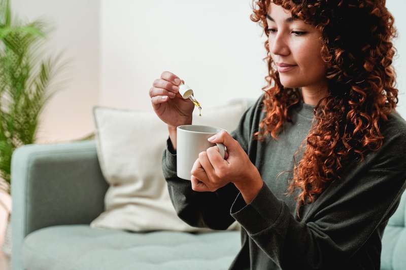 woman dropping cbd oil into a mug