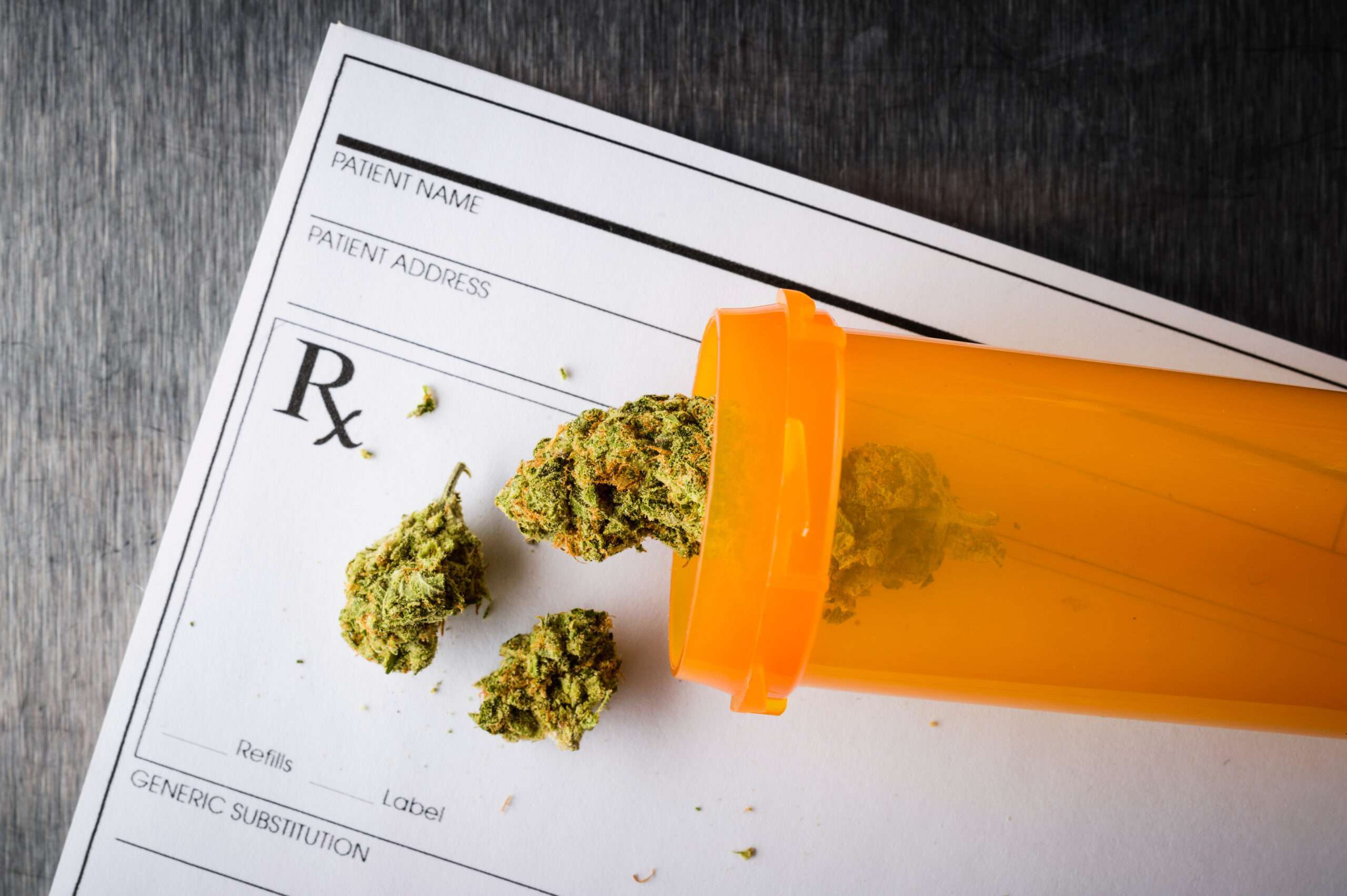prescription bottle with cannabis buds inside on top of prescription notepad
