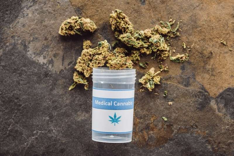 Top View of Medical Marijuana Buds Near Container on Marble Surface