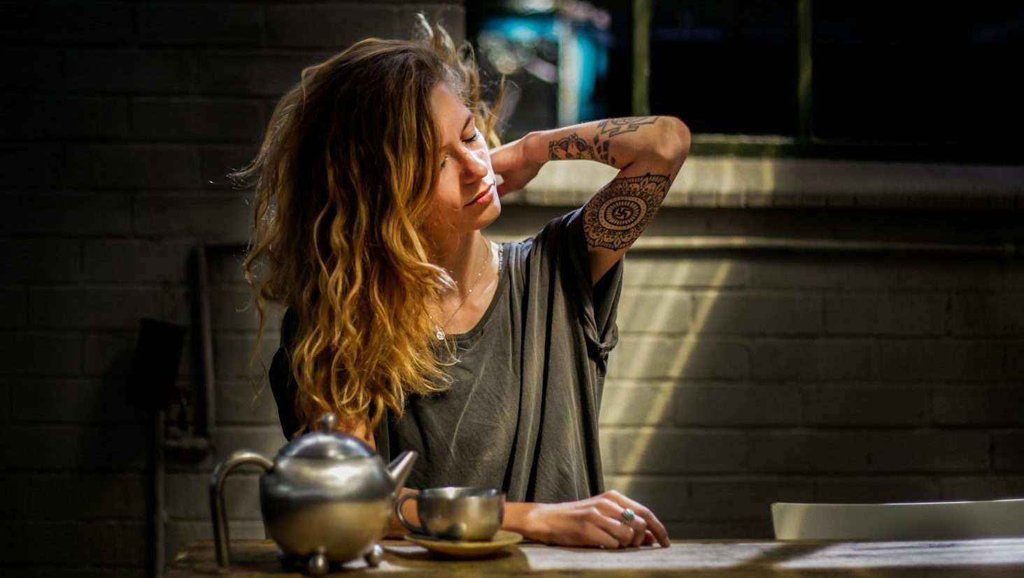 woman in gray top sitting beside gray tea pot and cup on brown wooden table